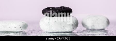 Panoramic shot of zen stones with water drops on wet glass on purple background Stock Photo