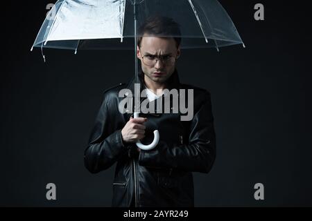 angry stylish brutal man in biker jacket with umbrella isolated on black Stock Photo