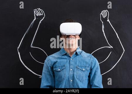 happy young man using virtual reality headset, with muscular arms drawing on blackboard Stock Photo
