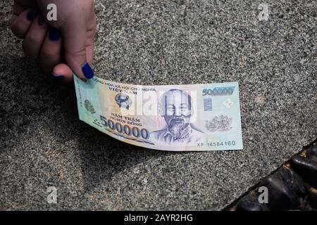 A hand picking up a piece of 50000 dong Vietnam money note on the floor. Stock Photo