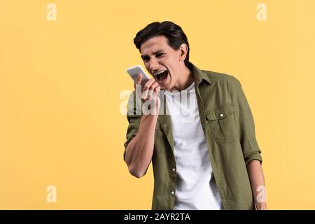 angry young man screaming at smartphone, isolated on yellow Stock Photo
