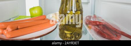 Panoramic shot of sausages, pickles and chili peppers in fridge with open door isolated on white,stock image Stock Photo