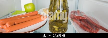 Panoramic shot of sausages with pickles and chili peppers in fridge with open door isolated on white,stock image Stock Photo