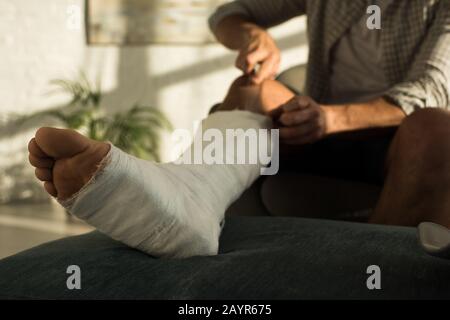 Selective focus of man scratching broken leg with ruler while sitting in armchair Stock Photo