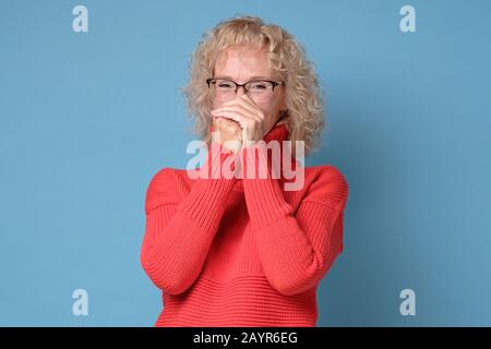 Beautiful middle age woman wearing red sweater and glasses trying to stop laughing because of funny crazy joke. Happy expression. Stock Photo