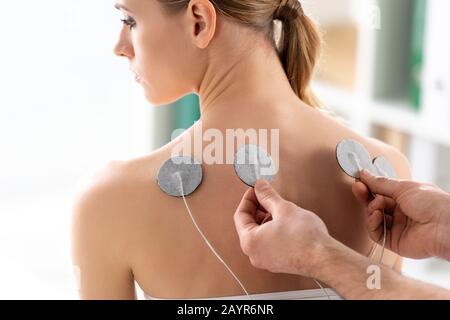 Therapist setting electrodes on back of beautiful woman during electrode treatment Stock Photo