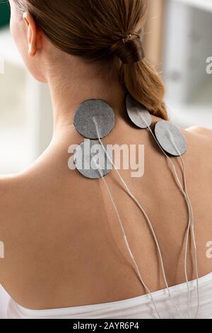 Back view of electrodes of neck of young woman during electrode treatment in clinic