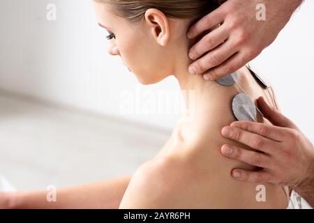 Side view of doctor setting electrodes on patient neck during electrode treatment in clinic Stock Photo