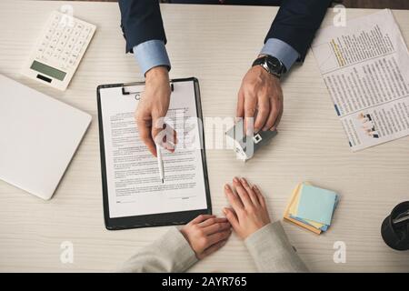 top view of agent giving pen to woman while touching house model Stock Photo