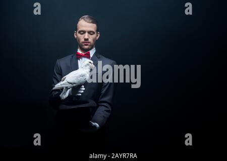 young magician showing trick with dove and hat in dark room with smoke Stock Photo