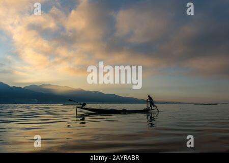 Before sunrise a leg-rowing fisherman in his boat is pulling in his fishing net he set the day before on Inle Lake in Myanmar. Stock Photo