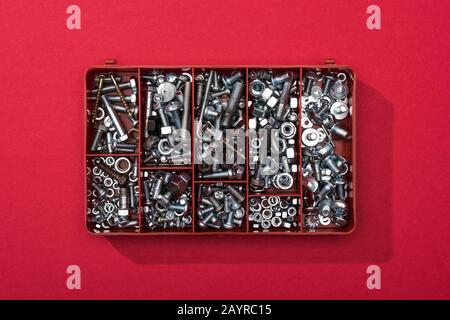 Top view of metal nuts and wood screws in tool box on red background Stock Photo