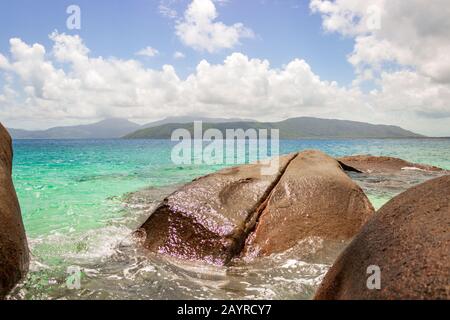 Nudey Beach, Fitzroy Island, rocks break through the crystal clear waters of the Coral Sea with the coast of Queensland Australia in the background. Stock Photo