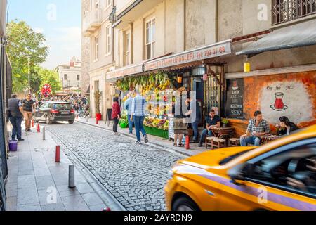 A busy street in the Galata Karakoy district of Istanbul Turkey with fruit stand, cafe, tourists, Turks and a speeding taxi, in Istanbul Turkey. Stock Photo