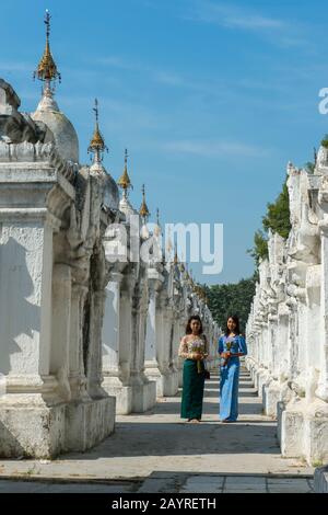 Two young local women at the rows of stupas each housing one of the 729 slabs engraved with the Buddhist teachings at the Kuthodaw Pagoda on Mandalay Stock Photo