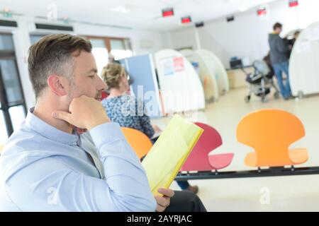 man reading forms on yellow paper while in waiting room Stock Photo