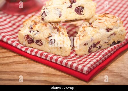 Three home made cranberry, lemon and almond scones resting on two tea towels with a red mug in the background Stock Photo