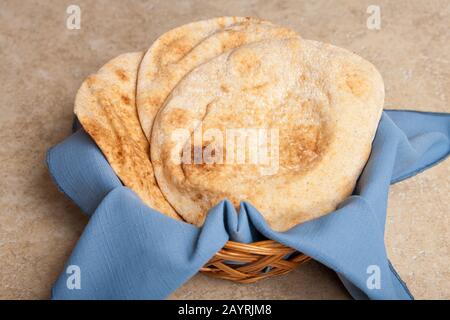 Three round pita loaves of bread in a wicker basket with a blue cloth napkin Stock Photo