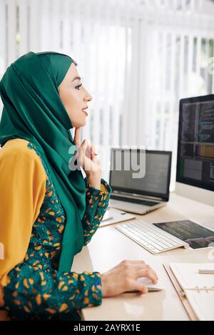 Excited female programmer sitting at office desk and writing code for mobile application Stock Photo
