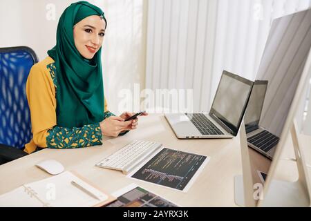 Pretty female software developer texting coworker after checking programming code for new mobile application Stock Photo