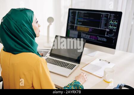 Serious female software engineer working on computer and laptop in her office Stock Photo