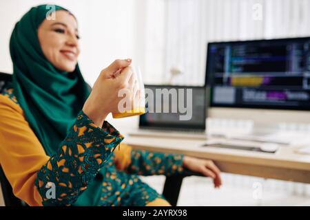 Happy young woman in traditional muslim dress drinking cup of coffee after finishing project Stock Photo