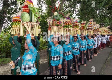 Bali, Indonesia - July 26, 2010: Group of women in traditional costumes and colourful offering on their heads walk to the holy Pura Tanah Lot temple. Stock Photo