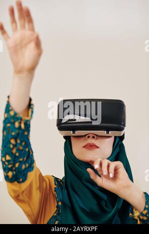 Young muslim woman in virtual reality headset testing new application Stock Photo