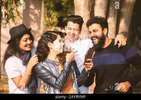 Group of young people laughing by seeing into smartphone - Millennials having fun with friends - trendy modern youth busy on mobile phone, Internet Stock Photo