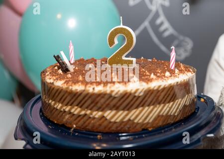 Chocolate birthday cake surrounded by confetti with lit candle for a second birthday or anniversary celebration Stock Photo