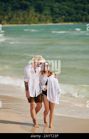 Young man hugging his girlfriend when they are walking on beach together on summer day Stock Photo
