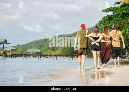 Hugging friends walking on beach of tropical island in the morning Stock Photo