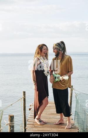 Man playing ukulele and singing for his beautiful happy wife when they are spending honeymoon by sea Stock Photo