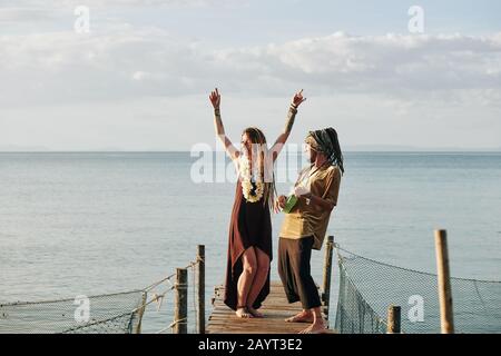 Cheerful man playing ukulele when his wife dancing on wooden pier Stock Photo