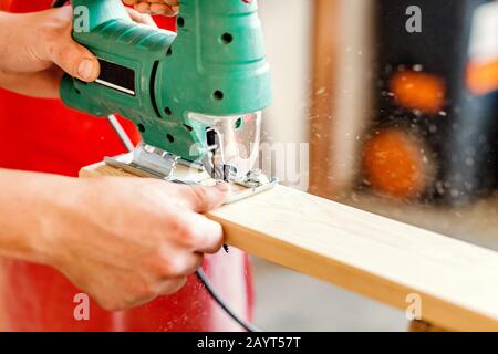 Close-up on worker cutting out a patterned contour on a wooden board using an electric jigsaw with a laser guide Stock Photo