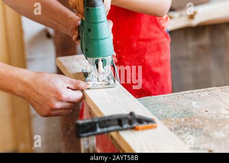 Close-up on worker cutting out a patterned contour on a wooden board using an electric jigsaw with a laser guide Stock Photo