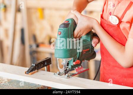 Close-up on worker cutting out a patterned contour on a wooden board using an electric jigsaw with a laser guide Stock Photo