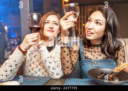Two girl friends have fun and chat while drinking a glass of wine in a restaurant in a nightclub. The concept of relaxing and frienship Stock Photo