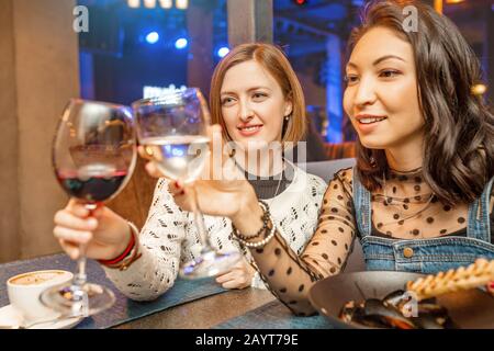 Two girl friends have fun and chat while drinking a glass of wine in a restaurant in a nightclub. The concept of relaxing and frienship Stock Photo