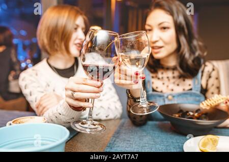 Two girl friends have fun and chat while drinking a glass of wine in a restaurant in a nightclub. The concept of relaxing and frienship Stock Photo