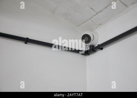White round cctv camera installed in the corner on a white wall. Minimalism. Corner. Stock Photo