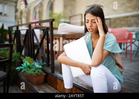 Frustrated sad young woman feeling tired worried about problem sitting with laptop Stock Photo