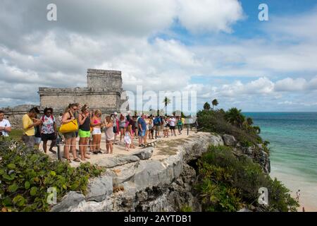 Tourists with the Castillo (castle) in background sightseeing at Tulum, which is the site of a Pre-Columbian Mayan walled city along the east coast of Stock Photo