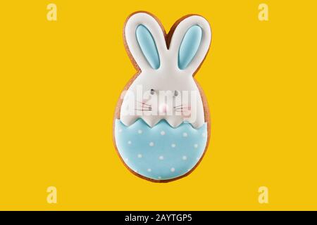 Cute white and blue bunny gingerbread isolated over vivid yellow background. Delicious frosted biscuit in form of pretty animal with copy space. Easter concept. Stock Photo