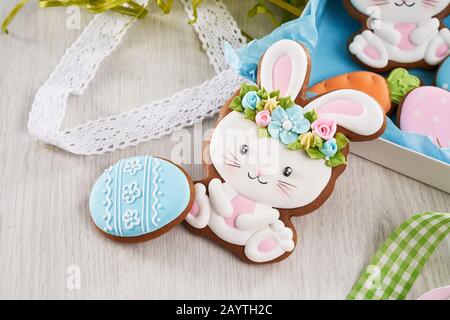 Painted easter bunny and blue egg gingerbreads lying near gift box with colorful ribbons. Tasty present for festive table. Wooden background Stock Photo