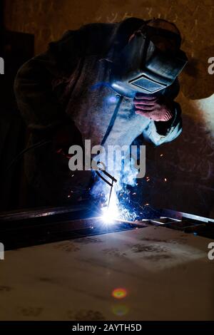 worker in protective uniform and mask welding metal. man using electric welding machine Stock Photo