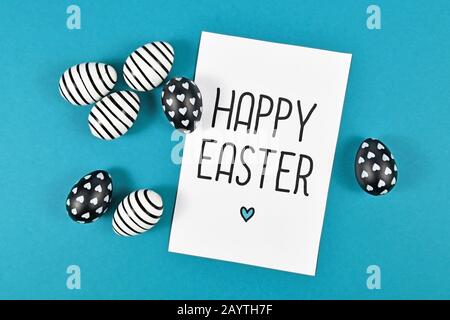 Easter eggs with simple black and white stripe and dot paintings with white card with 'Happy Easter' text on blue background Stock Photo