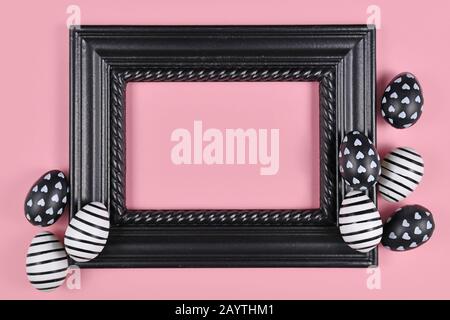 Easter design with blank black elegant picture frame surrounded by modern black and white easter eggs on pink background Stock Photo