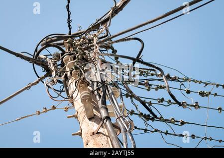 Electrical and telephone cables and coming together in a massive tangle on a wooden utility post against blue sky Stock Photo