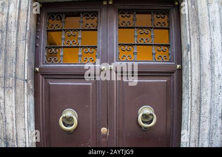 Close up of closed wooden door with metal door knobs, handles and cast iron lattice work above entrance. Italian architecture details background Stock Photo